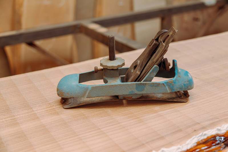 Two hands adjusting a quick-release bar clamp on a maple workpiece; close focus showing textured grip and machined steel hinge